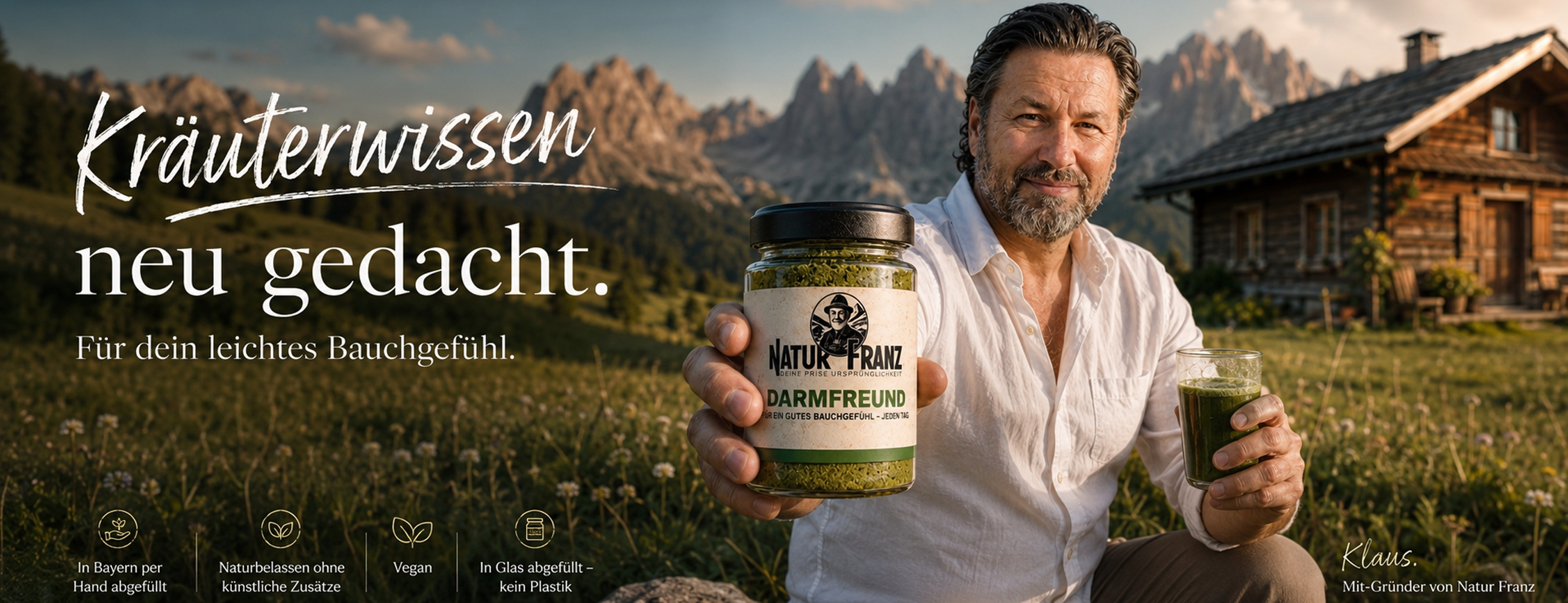 Mit-Gründer Klaus sitzt auf einer grünen Almwiese vor einem markanten Alpenpanorama und einer Holzalmhütte. Er hält in der linken Hand das Produktglas Darmfreund von Natur Franz, in der rechten Hand ein Glas mit grünem Kräuter-Shot mit Strohhalm. Links im Bild der handgeschriebene Slogan: Altes Kräuterwissen. Neu entdeckt. Im unteren Bildbereich vier Icons mit den Markenversprechen: nachhaltig und per Hand in Glas abgefüllt, 100% vegan, keine künstlichen Aromen oder Zusatzstoffe, Familienunternehmen